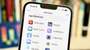 Photograph of the App Shortcuts feature open on an iPhone, with a bookshelf in the background showing the corner of Shortcuts' original logo as the Workflow app as artwork on the shelf.